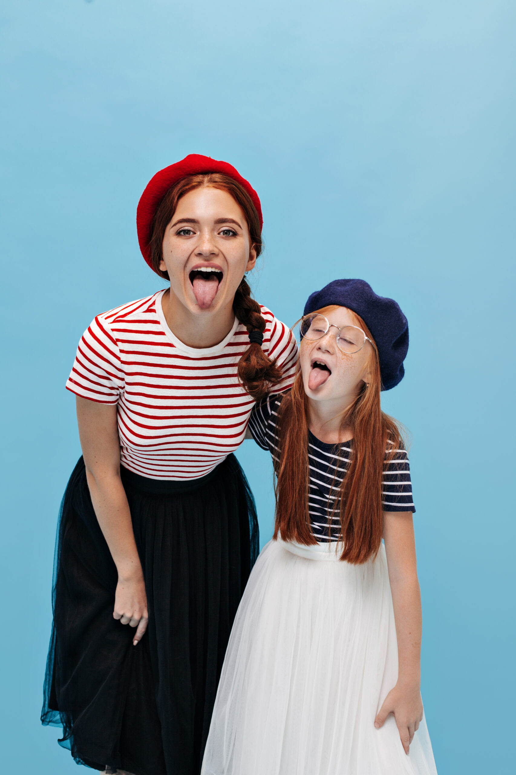 stylish-red-haired-young-women-bright-berets-cool-skirts-stylish-tshirts-showing-tongues-isolated-blue-background-scaled.jpg